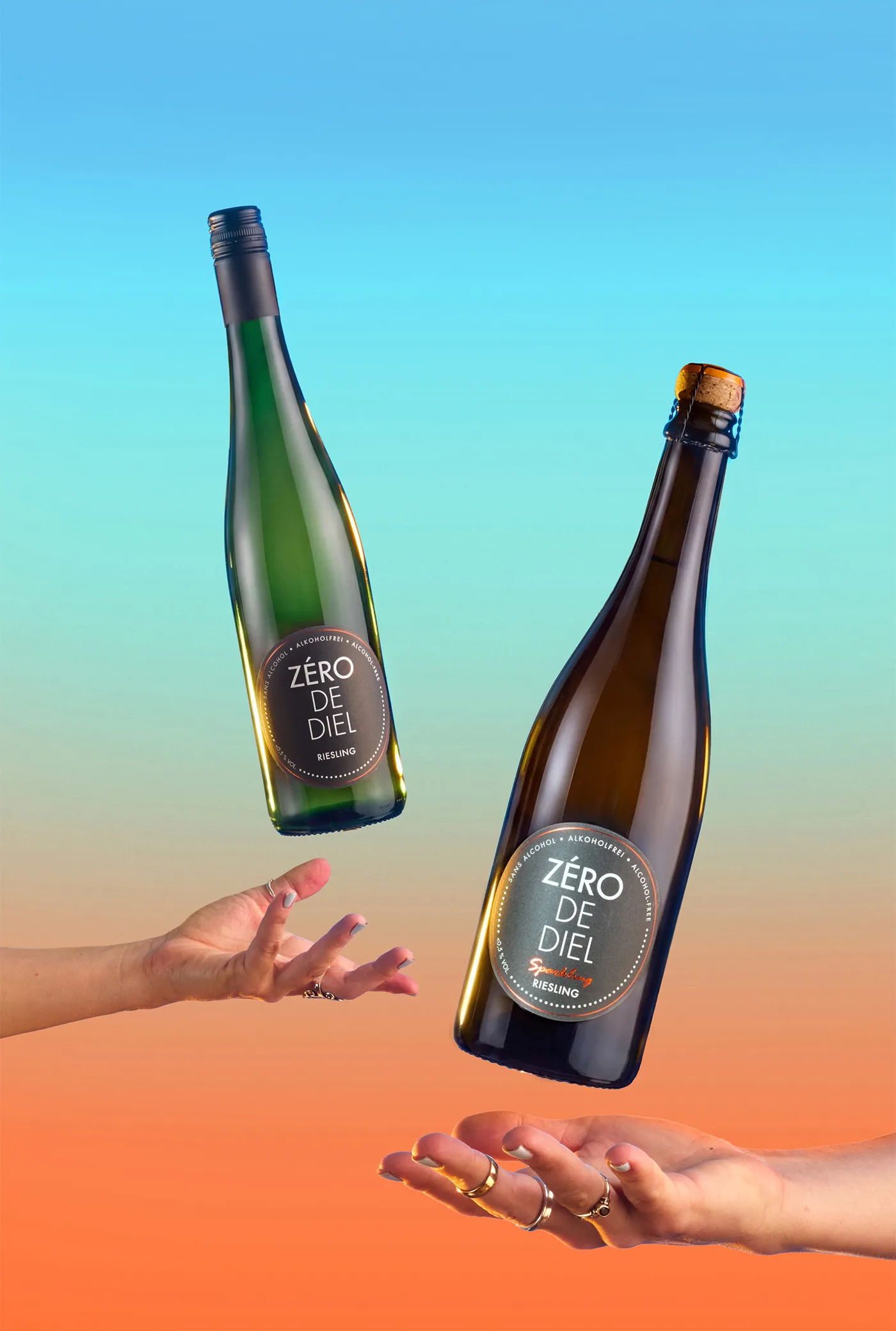 Two Zéro de Diel alcohol free Riesling bottles tossed between hands against a blue and orange gradient